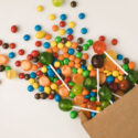 close-up view of colorful tasty candies in paper bag on white